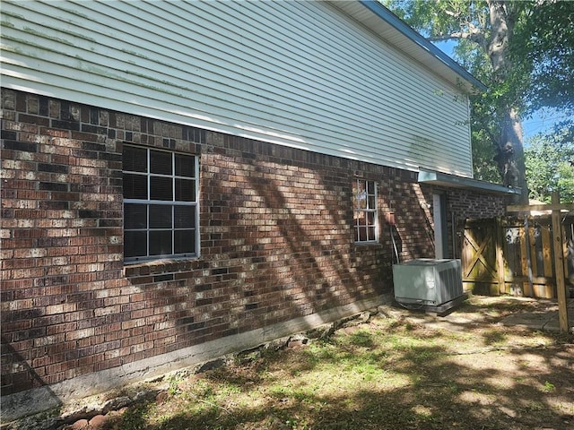 view of side of home with fence, central AC unit, and brick siding