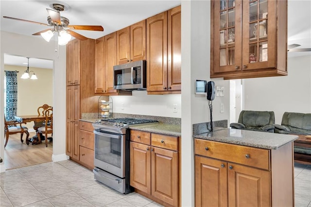 5245 Sanford St, Metairie, LA 70006 - kitchen featuring appliances with stainless steel finishes, a ceiling fan, brown cabinets, glass insert cabinets, and light tile patterned flooring