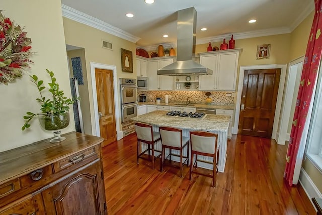 kitchen featuring a breakfast bar, stainless steel appliances, island range hood, visible vents, and ornamental molding
