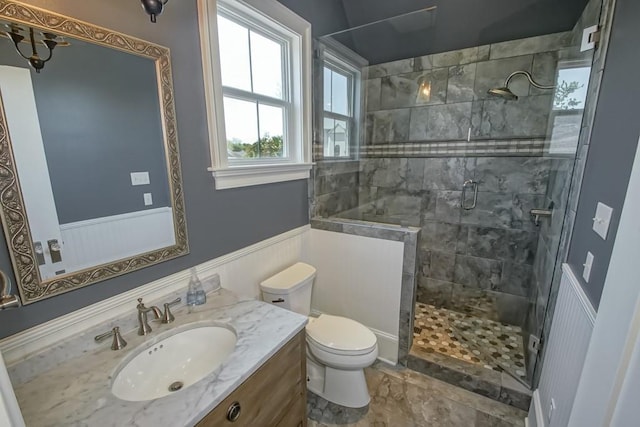 full bath featuring a stall shower, vanity, toilet, and a wainscoted wall