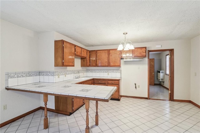 2617 Danneel St, New Orleans, LA 70113 - kitchen featuring a notable chandelier, heating unit, brown cabinetry, tile countertops, and a sink