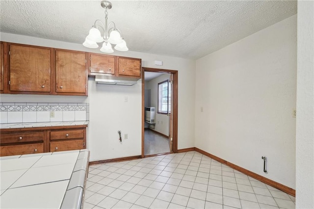 2617 Danneel St, New Orleans, LA 70113 - kitchen featuring tile countertops, brown cabinetry, a textured ceiling, a notable chandelier, and backsplash