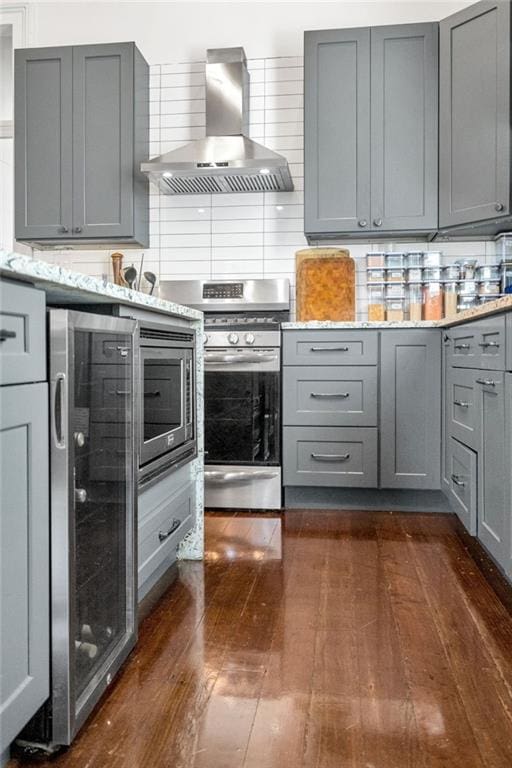 kitchen with gray cabinets, backsplash, wall chimney exhaust hood, dark wood finished floors, and stainless steel gas stove