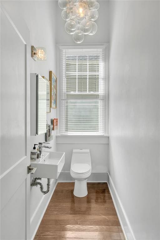 half bathroom featuring baseboards, a sink, toilet, a chandelier, and wood finished floors