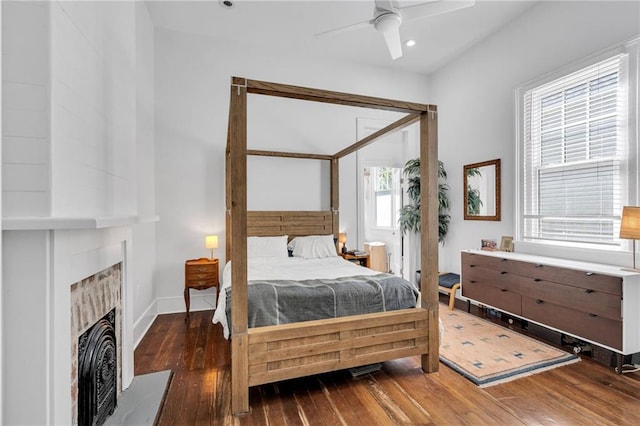 bedroom featuring baseboards, a fireplace with raised hearth, ceiling fan, recessed lighting, and hardwood / wood-style floors