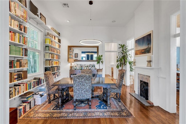dining space featuring a brick fireplace, visible vents, and wood finished floors