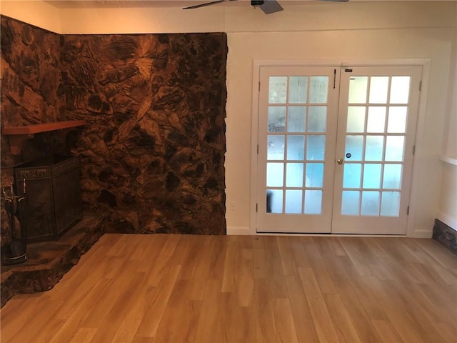 interior space featuring a ceiling fan, wood finished floors, a fireplace with raised hearth, french doors, and baseboards