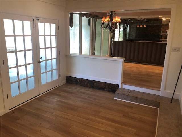 unfurnished dining area featuring french doors, a chandelier, wood finished floors, and baseboards