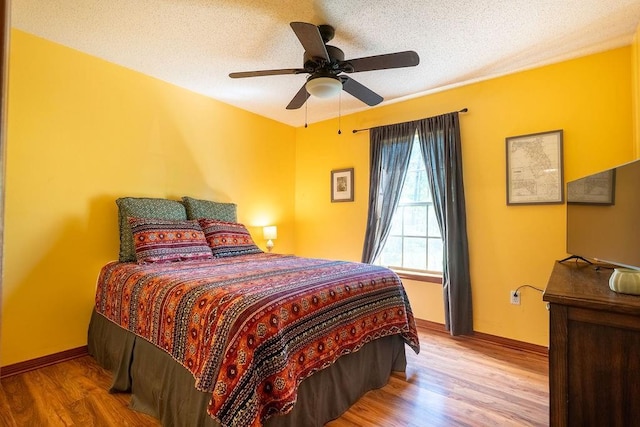 bedroom with a textured ceiling, wood finished floors, baseboards, and a ceiling fan