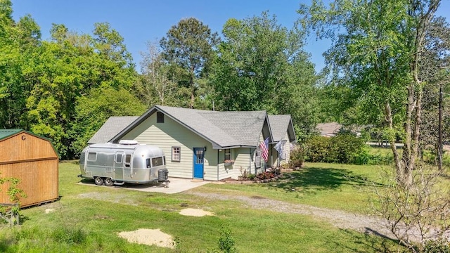 view of front of property featuring a front yard, a storage unit, an outbuilding, driveway, and roof with shingles
