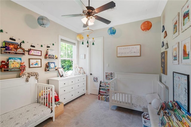 bedroom featuring a nursery area, ceiling fan, and light carpet
