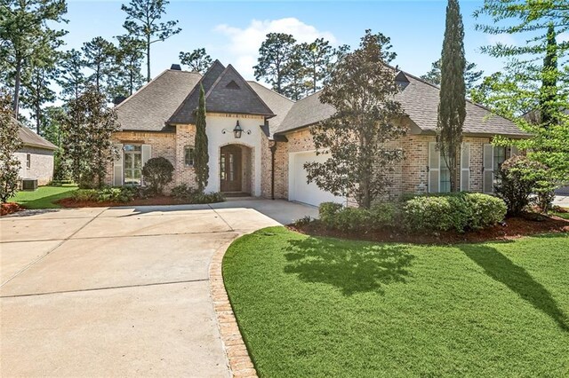french country home with a shingled roof, a garage, concrete driveway, brick siding, and a front lawn