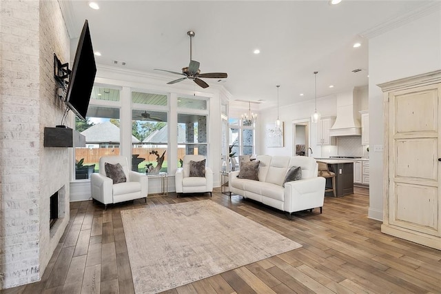 living area featuring ceiling fan with notable chandelier, hardwood / wood-style flooring, a large fireplace, and ornamental molding