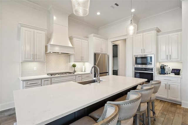kitchen with white cabinets, an island with sink, a kitchen breakfast bar, stainless steel appliances, and a sink