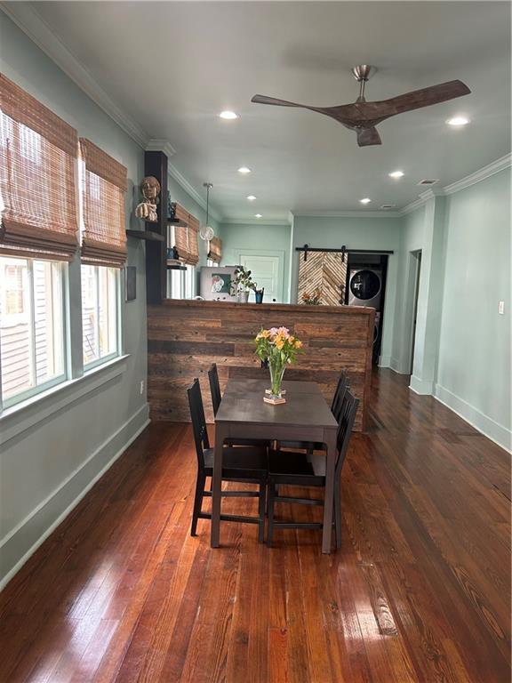 dining space with a ceiling fan, stacked washer / drying machine, baseboards, dark wood finished floors, and crown molding