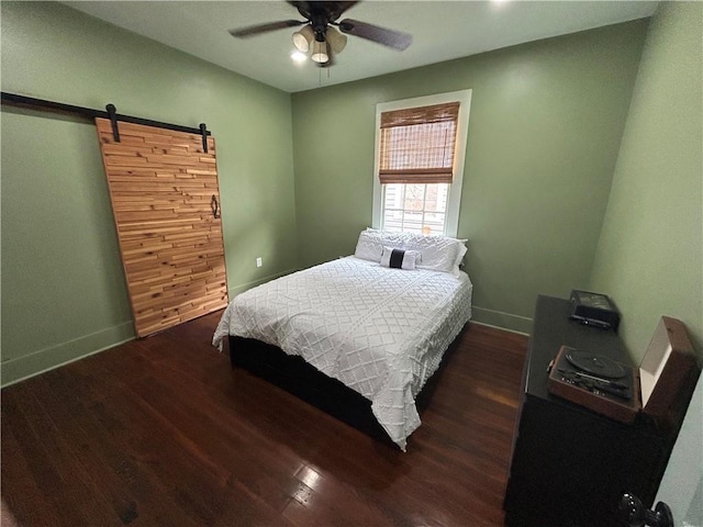 bedroom with wood finished floors, baseboards, a barn door, and ceiling fan