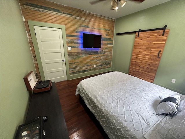 bedroom featuring an accent wall, wood finished floors, a barn door, baseboards, and wood walls