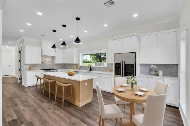 kitchen with stainless steel fridge with ice dispenser, ornamental molding, visible vents, a sink, and custom range hood