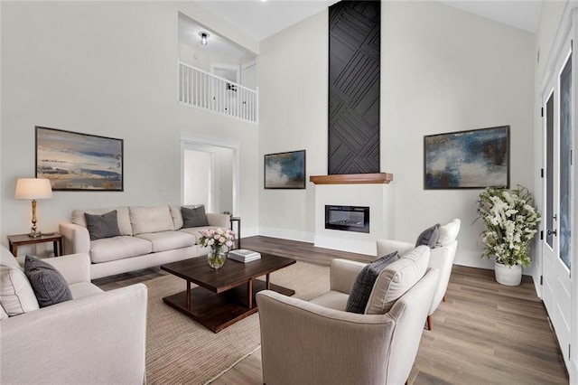 living room with a glass covered fireplace, a high ceiling, baseboards, and wood finished floors