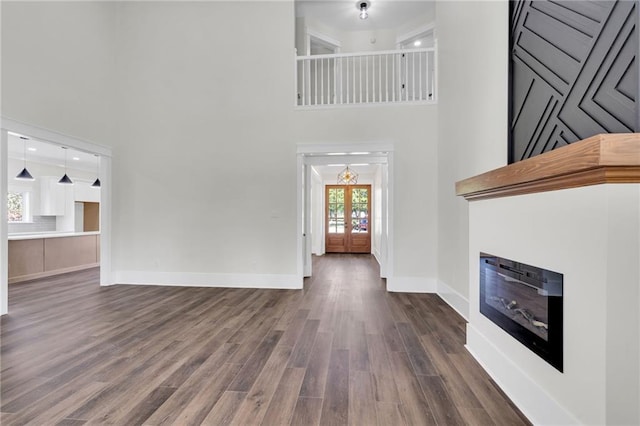unfurnished living room with dark wood-type flooring, french doors, a high ceiling, and baseboards
