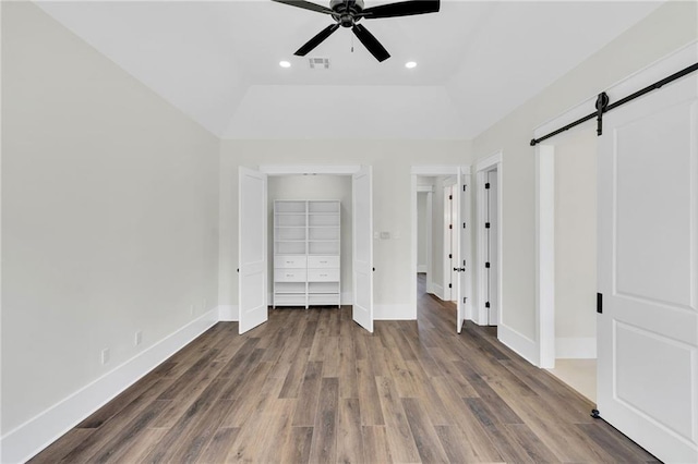 unfurnished bedroom with wood finished floors, baseboards, visible vents, and a barn door