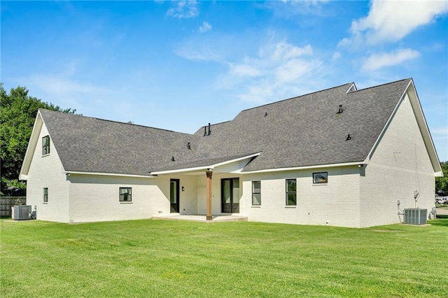 back of house with central AC, a lawn, roof with shingles, a patio area, and brick siding