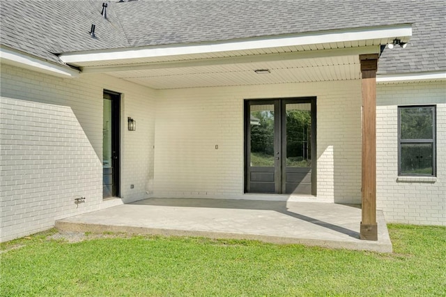 exterior space with french doors, a shingled roof, a patio area, and brick siding