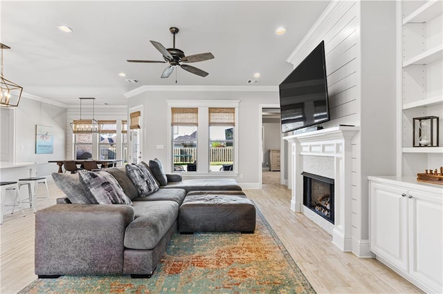 living room featuring ornamental molding, light wood-style floors, a fireplace, recessed lighting, and ceiling fan with notable chandelier