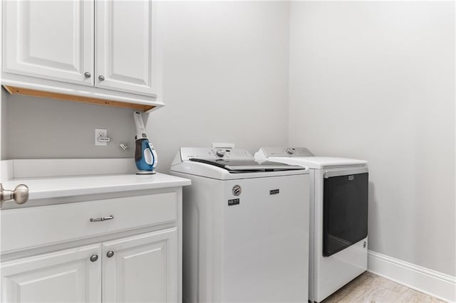 laundry area with cabinet space, baseboards, light wood finished floors, and washing machine and dryer