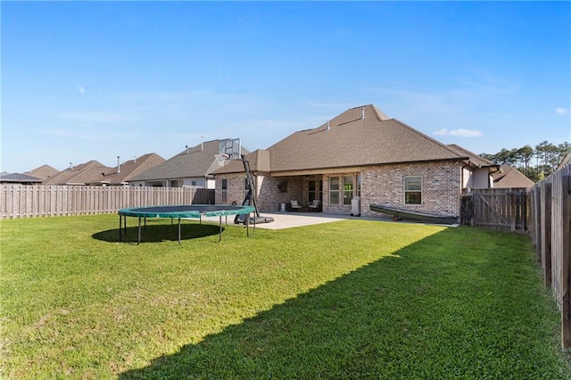 rear view of property with a patio area, a trampoline, a lawn, a fenced backyard, and brick siding