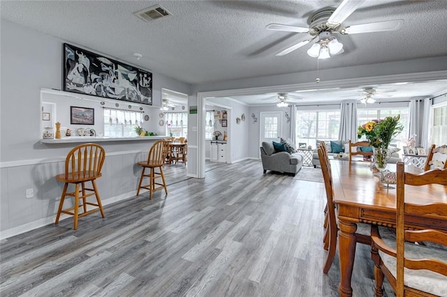 232 Chateau Dr, Slidell, LA 70460 - dining space with ceiling fan, light wood-type flooring, a textured ceiling, a bar, and a wainscoted wall