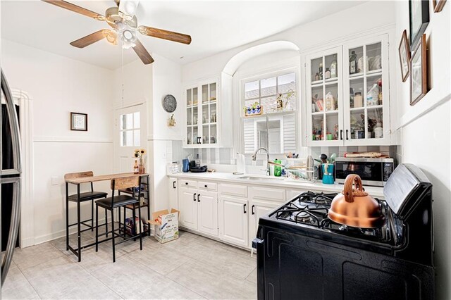 8632 Apple St, New Orleans, LA 70118 - kitchen featuring ceiling fan, light countertops, white cabinets, glass insert cabinets, and stainless steel appliances