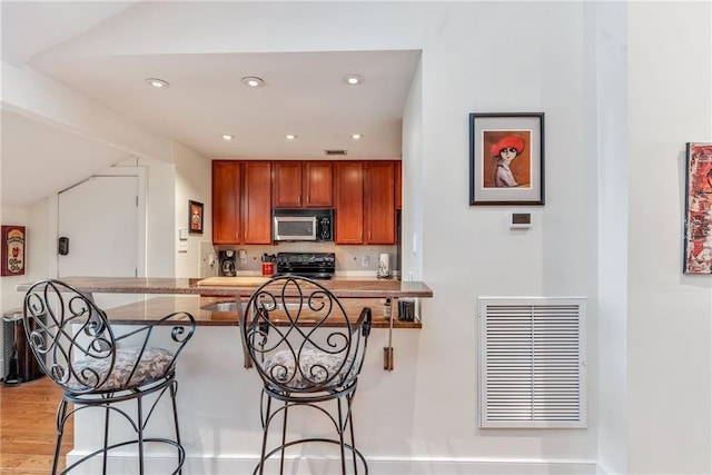 kitchen featuring stainless steel microwave, range, vaulted ceiling, visible vents, and a breakfast bar area