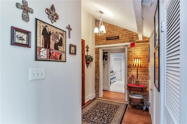 corridor featuring brick wall, wood finished floors, an inviting chandelier, and vaulted ceiling