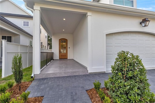 view of exterior entry featuring stucco siding, fence, and a garage