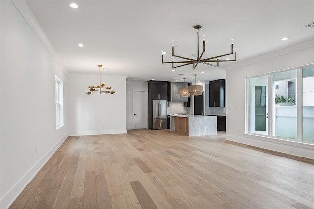 unfurnished living room with an inviting chandelier, crown molding, and light wood finished floors