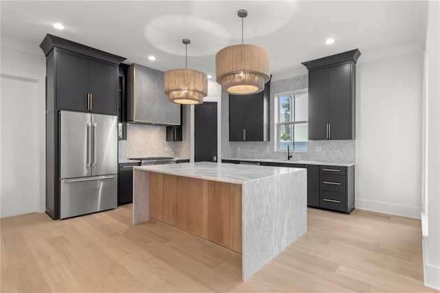 kitchen with custom range hood, decorative backsplash, light wood finished floors, and stainless steel appliances