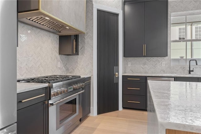 kitchen with light wood-type flooring, a sink, high end range, backsplash, and exhaust hood