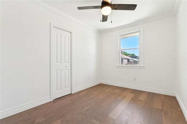 unfurnished bedroom featuring a closet, baseboards, crown molding, ceiling fan, and wood finished floors