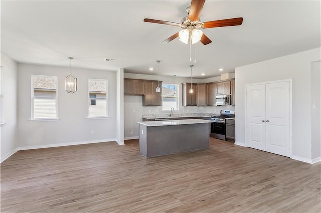 kitchen with baseboards, a center island, ceiling fan, light wood finished floors, and appliances with stainless steel finishes