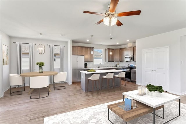 living area with light wood-type flooring, ceiling fan with notable chandelier, baseboards, and recessed lighting