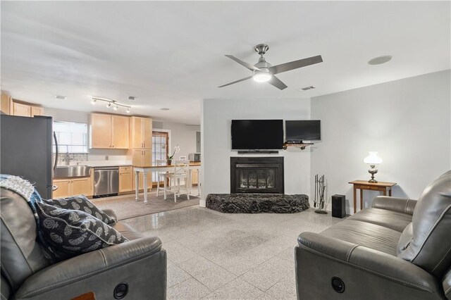living area featuring visible vents, a glass covered fireplace, and ceiling fan