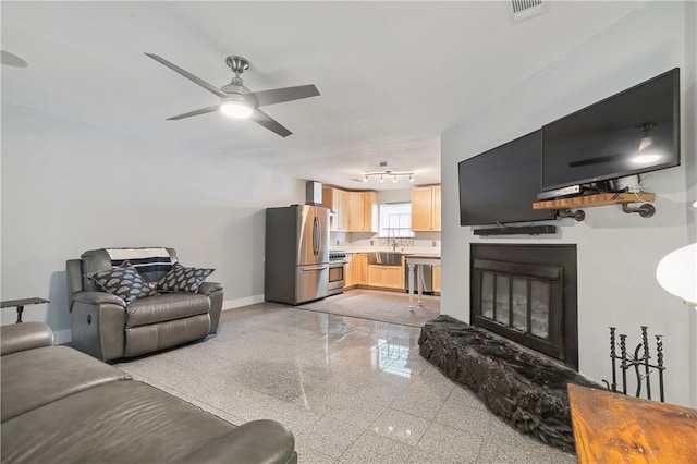 living area featuring ceiling fan, visible vents, granite finish floor, baseboards, and a glass covered fireplace