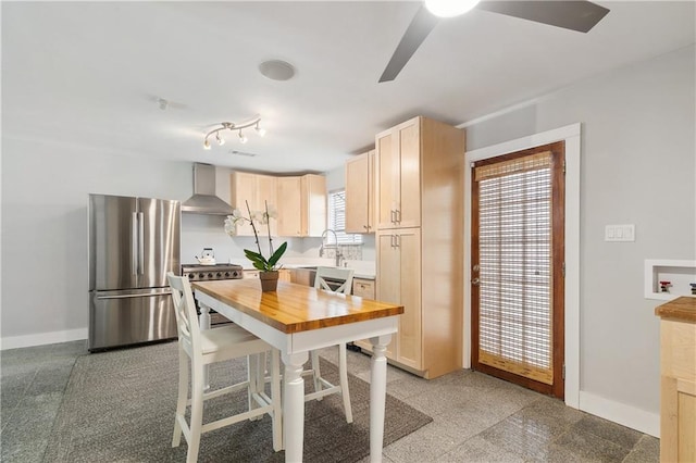 kitchen with ceiling fan, appliances with stainless steel finishes, wood counters, granite finish floor, and wall chimney exhaust hood