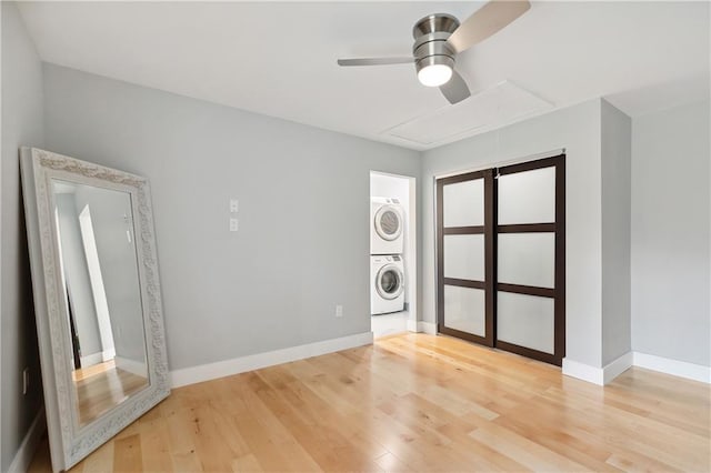spare room featuring light wood-style flooring, attic access, a ceiling fan, baseboards, and stacked washer and clothes dryer