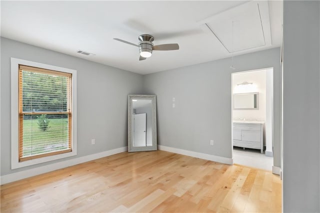 unfurnished bedroom with attic access, visible vents, baseboards, light wood finished floors, and ensuite bathroom