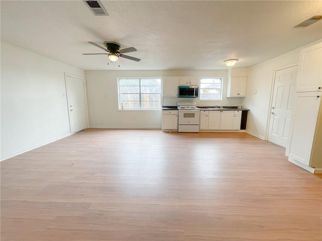 kitchen featuring light wood-type flooring, white cabinets, visible vents, white range with electric stovetop, and stainless steel microwave