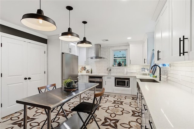 kitchen with decorative backsplash, white cabinets, a sink, stainless steel appliances, and wall chimney exhaust hood