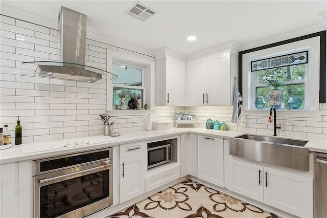 kitchen with decorative backsplash, appliances with stainless steel finishes, wall chimney range hood, a sink, and visible vents
