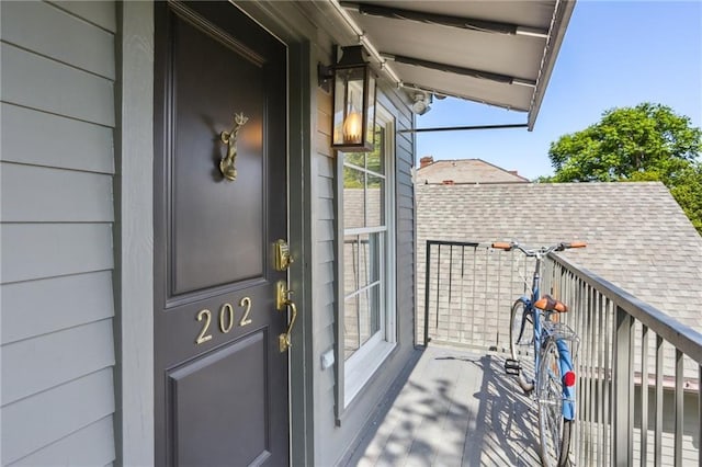 entrance to property with roof with shingles and a balcony